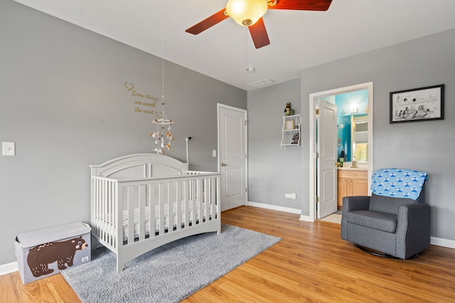 bedroom featuring ceiling fan, a crib, ensuite bathroom, and light hardwood / wood-style flooring