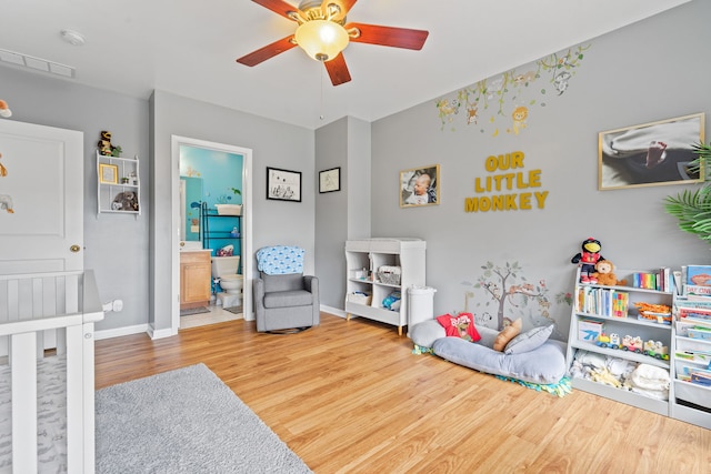 bedroom featuring a crib, ensuite bathroom, hardwood / wood-style flooring, and ceiling fan