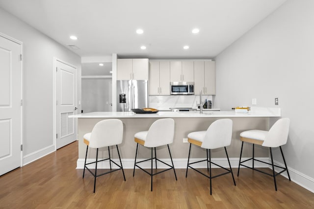 kitchen featuring a breakfast bar, a peninsula, stainless steel appliances, light countertops, and white cabinetry