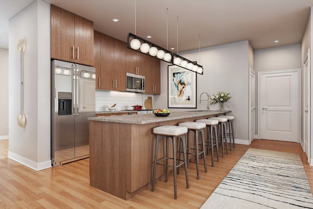 kitchen with light hardwood / wood-style flooring, a kitchen bar, kitchen peninsula, sink, and appliances with stainless steel finishes