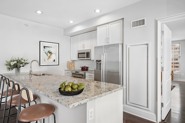 kitchen with a breakfast bar area, appliances with stainless steel finishes, sink, white cabinetry, and light stone counters