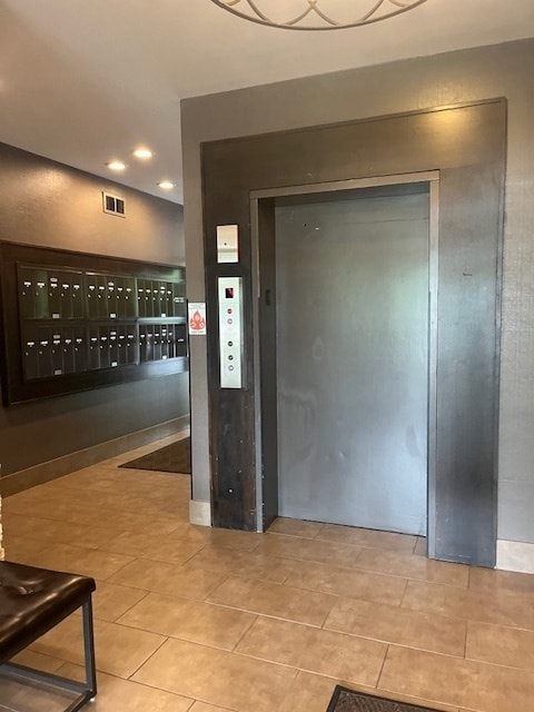 entryway featuring light tile patterned floors, elevator, and a mail area