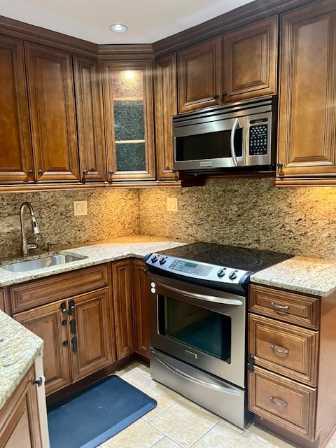 kitchen featuring backsplash, sink, light stone countertops, and appliances with stainless steel finishes