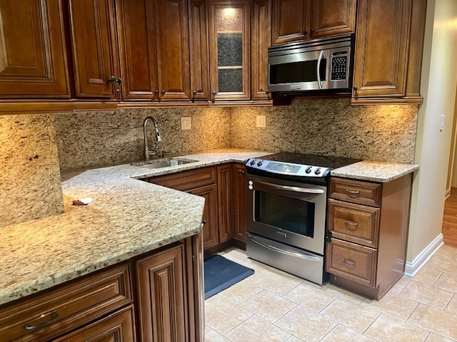 kitchen with appliances with stainless steel finishes, light stone countertops, tasteful backsplash, and sink