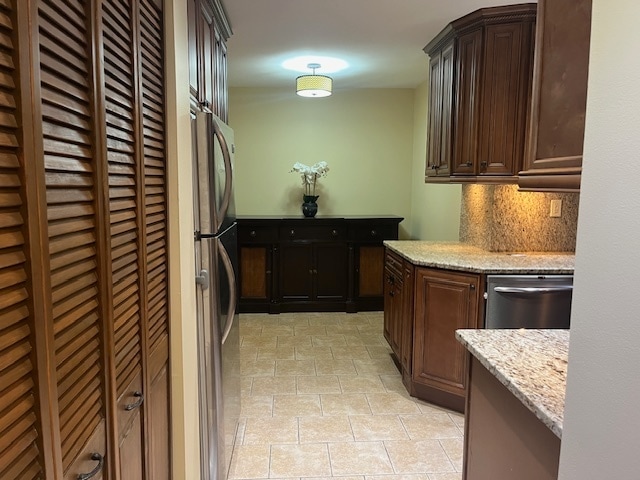 kitchen featuring appliances with stainless steel finishes, light stone counters, dark brown cabinets, and backsplash