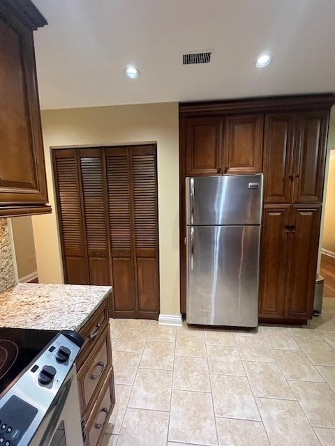 kitchen featuring stainless steel fridge, white range with electric stovetop, light tile patterned floors, and light stone countertops