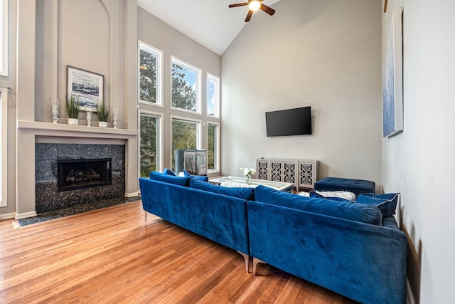 living room with ceiling fan, hardwood / wood-style flooring, a premium fireplace, and high vaulted ceiling