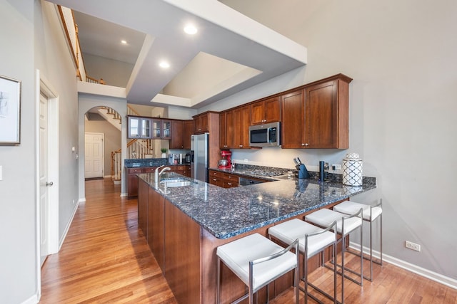 kitchen featuring dark stone counters, light hardwood / wood-style floors, kitchen peninsula, a kitchen bar, and stainless steel appliances