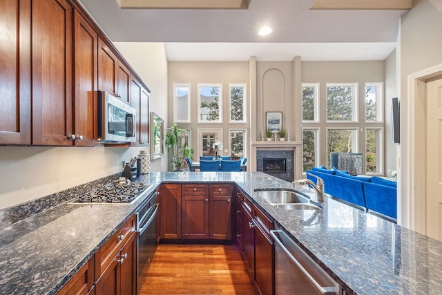 kitchen with kitchen peninsula, sink, light hardwood / wood-style flooring, stainless steel appliances, and dark stone counters