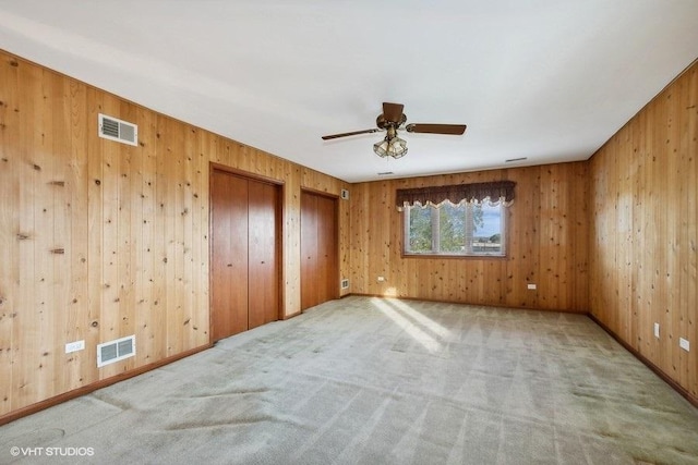 unfurnished bedroom featuring ceiling fan, light carpet, and multiple closets