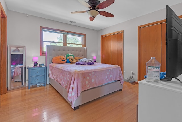 bedroom featuring multiple closets, light wood-type flooring, and ceiling fan