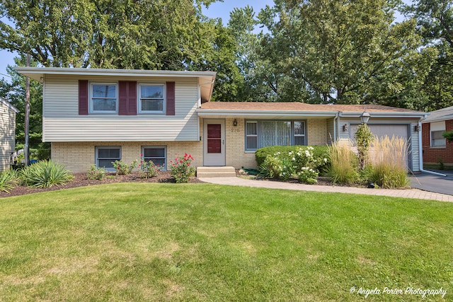 tri-level home featuring a garage, brick siding, driveway, and a front yard