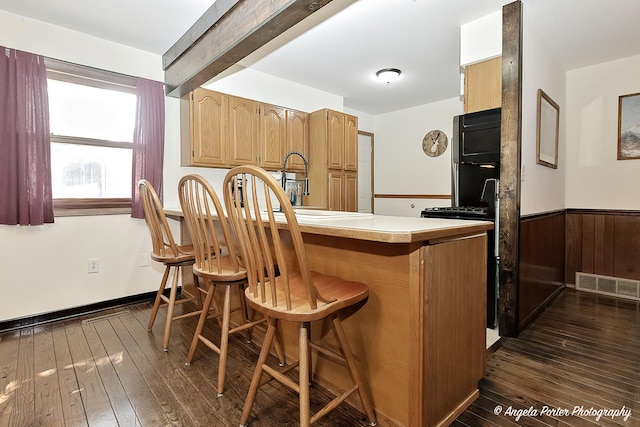 kitchen featuring visible vents, a wainscoted wall, a breakfast bar area, a peninsula, and light countertops