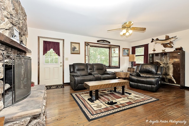 living room with a ceiling fan, wood finished floors, and a stone fireplace