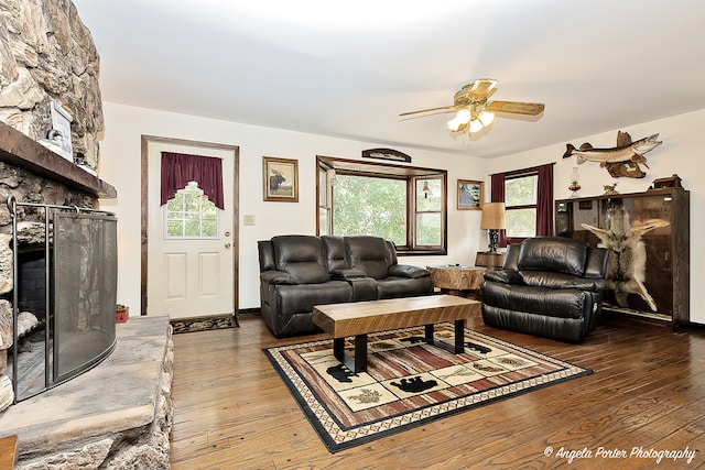 living room featuring ceiling fan, a stone fireplace, and wood finished floors