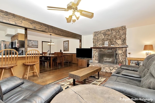 living room with light wood-type flooring, ceiling fan with notable chandelier, and a stone fireplace