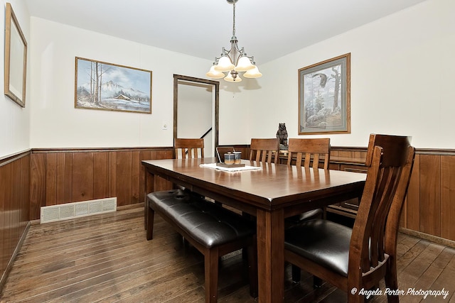 dining space featuring a notable chandelier, wood walls, visible vents, wainscoting, and dark wood-style floors