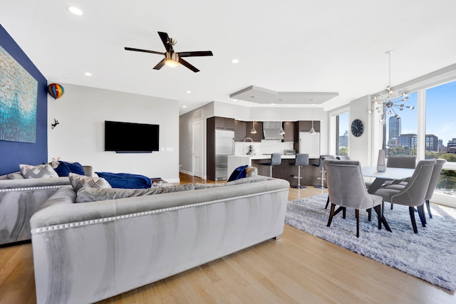 living room featuring ceiling fan with notable chandelier, sink, and light hardwood / wood-style flooring