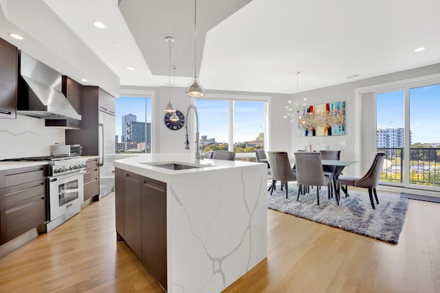 kitchen with a healthy amount of sunlight, wall chimney range hood, a center island with sink, and stainless steel stove