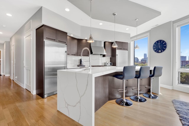 kitchen featuring dark brown cabinetry, wall chimney range hood, built in refrigerator, and plenty of natural light