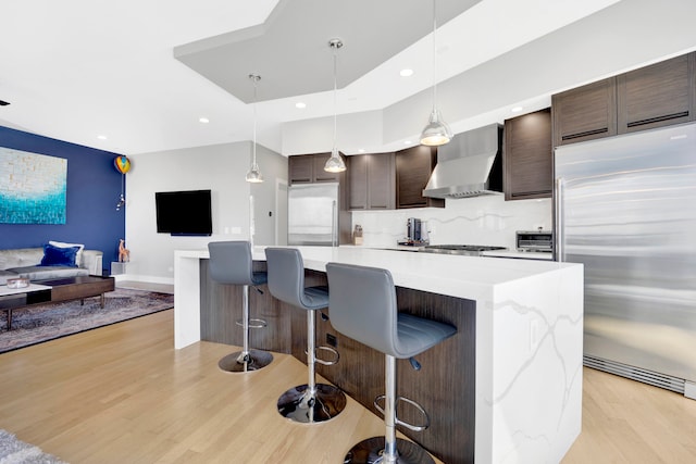 kitchen with appliances with stainless steel finishes, light wood-type flooring, a kitchen island, and wall chimney range hood