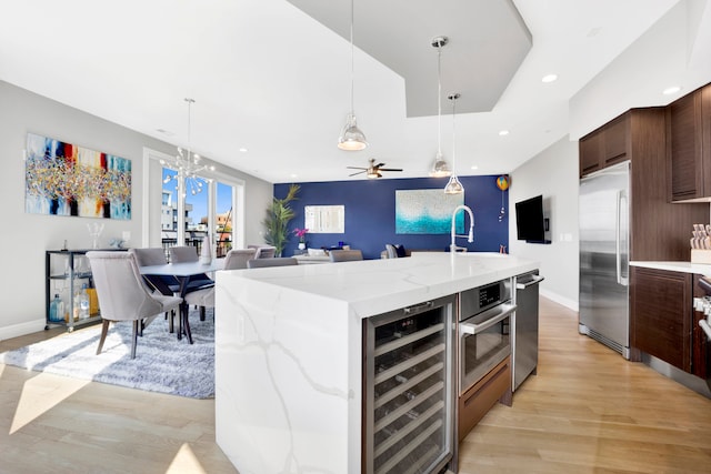 kitchen with light wood-type flooring, an island with sink, beverage cooler, and stainless steel appliances