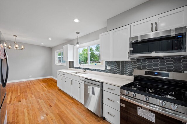 kitchen featuring pendant lighting, tasteful backsplash, white cabinets, light hardwood / wood-style flooring, and stainless steel appliances