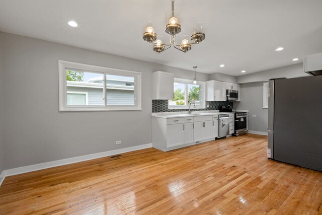 kitchen with appliances with stainless steel finishes, decorative backsplash, white cabinetry, light wood-type flooring, and decorative light fixtures