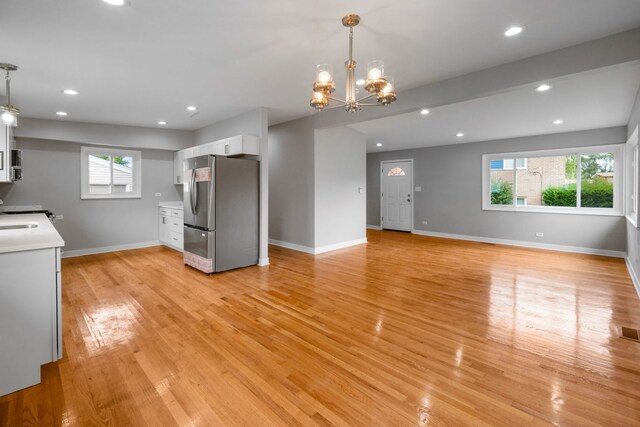 kitchen with white cabinets, hanging light fixtures, light wood-type flooring, and stainless steel refrigerator