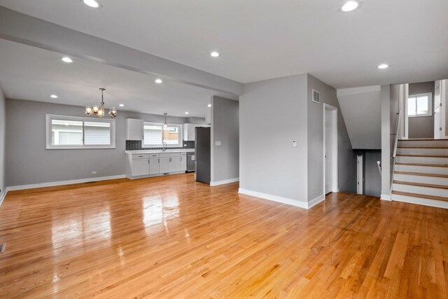 unfurnished living room with light wood-type flooring, an inviting chandelier, and sink