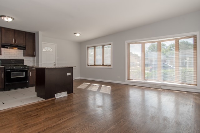 kitchen featuring light stone counters, dark brown cabinets, a center island, black range with gas cooktop, and light hardwood / wood-style flooring