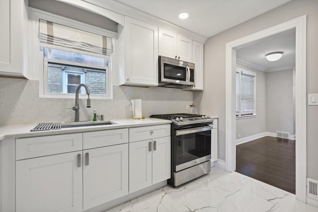 kitchen featuring white cabinetry, sink, stainless steel appliances, light hardwood / wood-style flooring, and ornamental molding