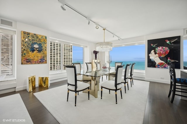 dining space with an inviting chandelier, a water view, track lighting, and dark wood-type flooring