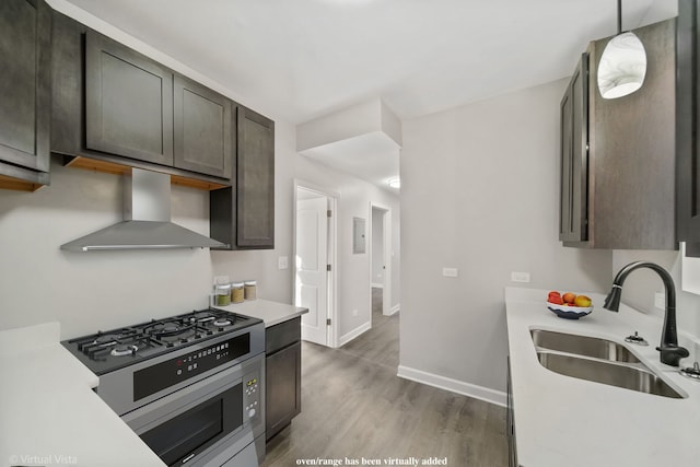 kitchen featuring light countertops, wall chimney exhaust hood, stainless steel range with gas cooktop, and a sink