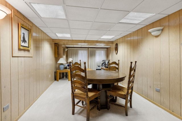 dining space with a drop ceiling and wooden walls