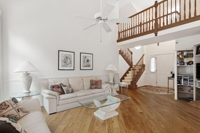 living room featuring ceiling fan, a towering ceiling, and wood-type flooring