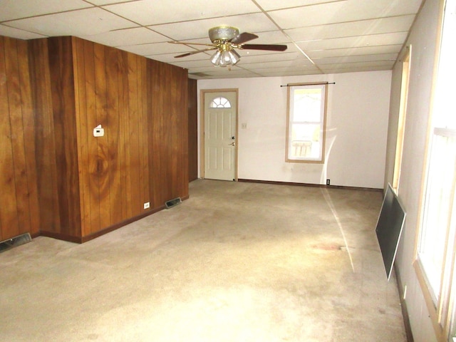 interior space with ceiling fan, light colored carpet, a drop ceiling, and wood walls