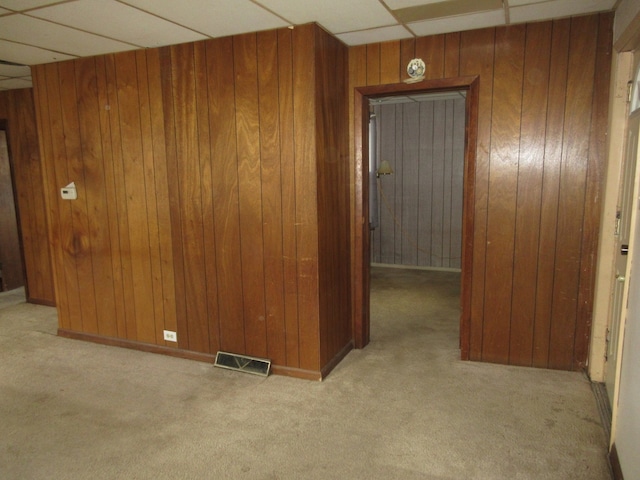 carpeted empty room featuring a drop ceiling and wooden walls