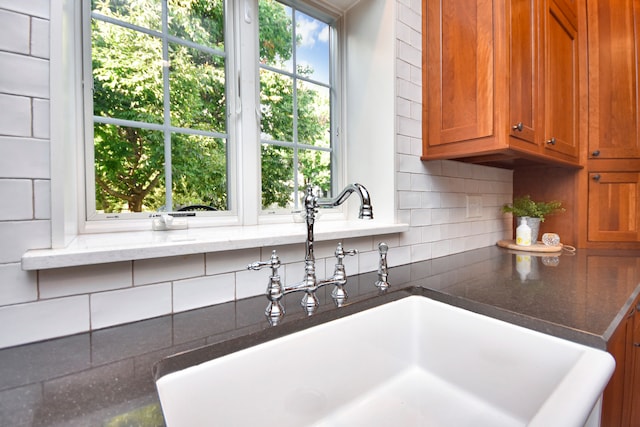 kitchen with decorative backsplash, a wealth of natural light, dark stone counters, and sink