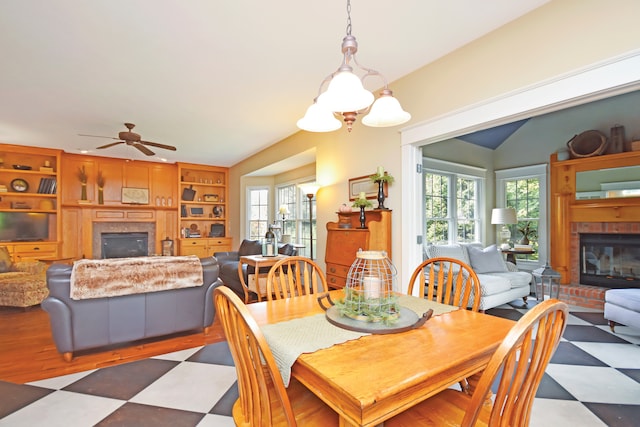 dining area featuring built in features, ceiling fan with notable chandelier, and a brick fireplace