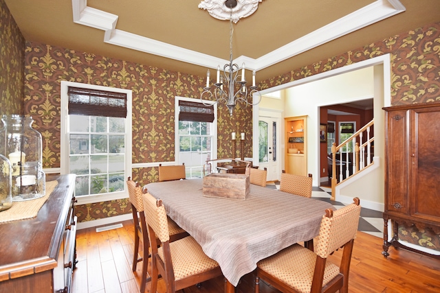 dining area with a chandelier, hardwood / wood-style floors, ornamental molding, and a raised ceiling