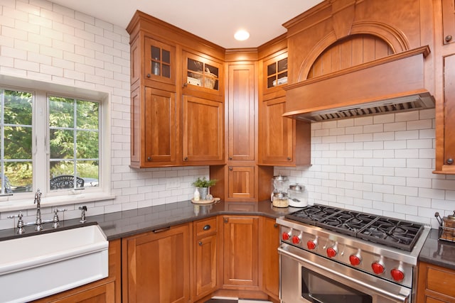 kitchen featuring premium range hood, luxury range, dark stone counters, sink, and decorative backsplash