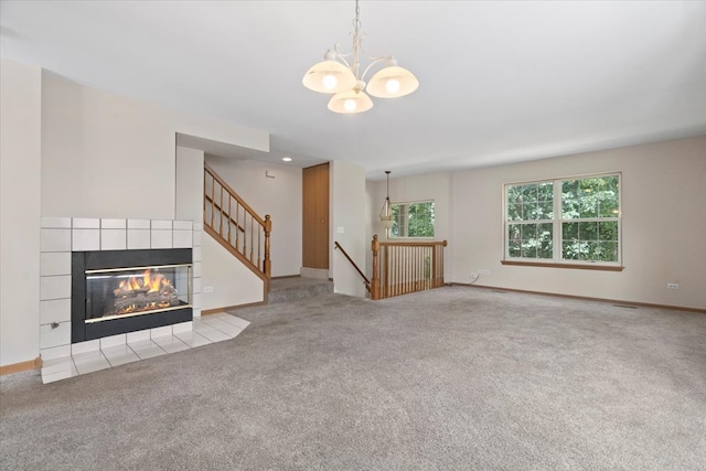 unfurnished living room with a tiled fireplace, light colored carpet, and a notable chandelier