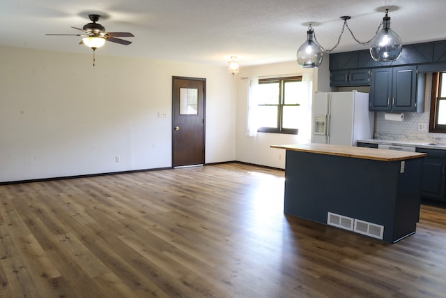 kitchen featuring white fridge with ice dispenser, dark hardwood / wood-style floors, hanging light fixtures, a kitchen island, and ceiling fan