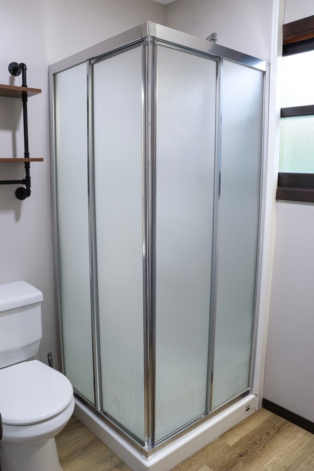 bathroom featuring hardwood / wood-style flooring, a shower with door, and toilet