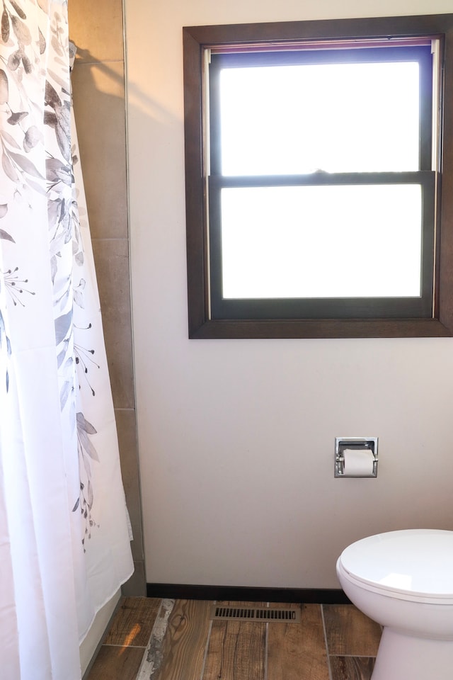 bathroom featuring a shower with shower curtain, hardwood / wood-style flooring, toilet, and a wealth of natural light