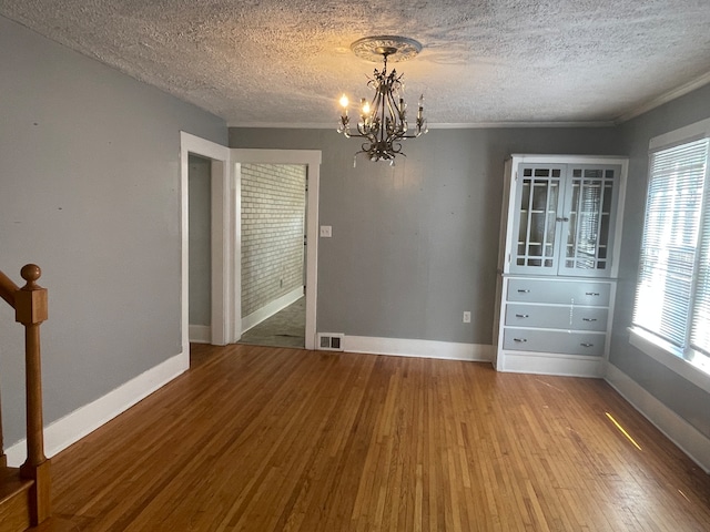 unfurnished bedroom with an inviting chandelier, multiple windows, hardwood / wood-style floors, and a textured ceiling