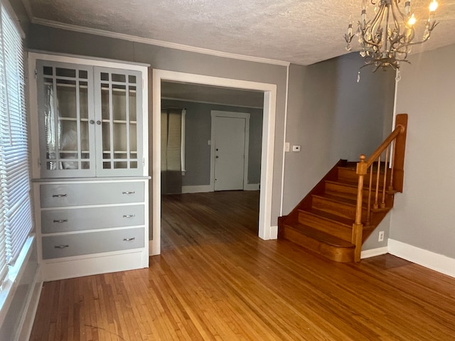 spare room with a textured ceiling, wood-type flooring, crown molding, and a notable chandelier