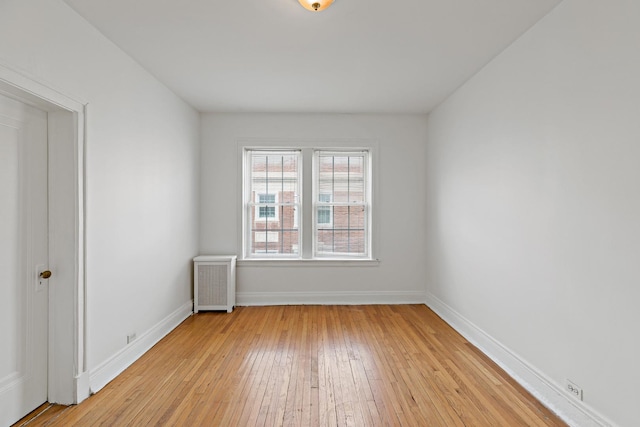 spare room with radiator, light wood finished floors, and baseboards