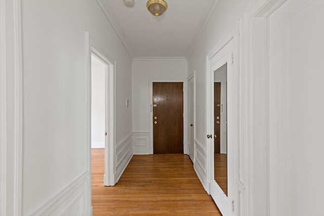 hall featuring light wood-style floors, a wainscoted wall, a decorative wall, and ornamental molding